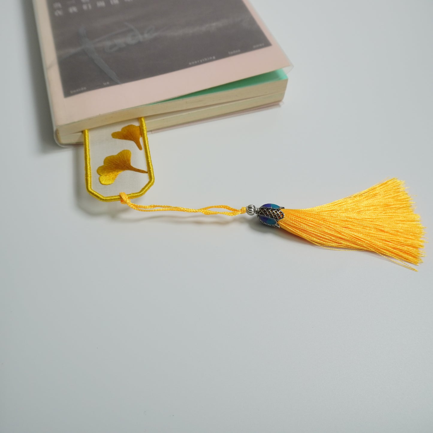 Hand-embroidered ginkgo leaf bookmark on silk with olive yellow tassel in book.