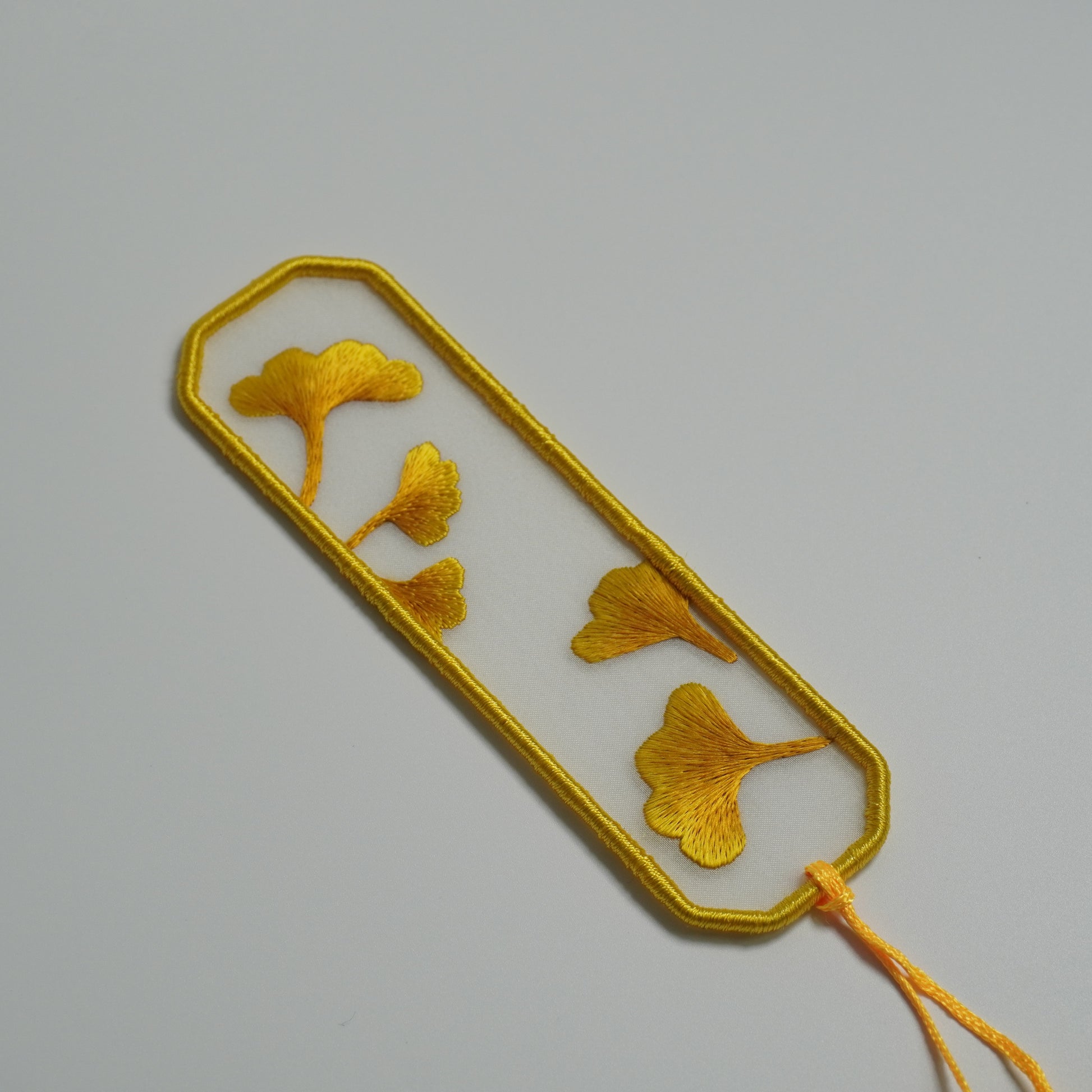 Details of Hand-embroidered ginkgo leaf bookmark on silk with olive yellow tassel. Traditional Chinese embroidery craft.
