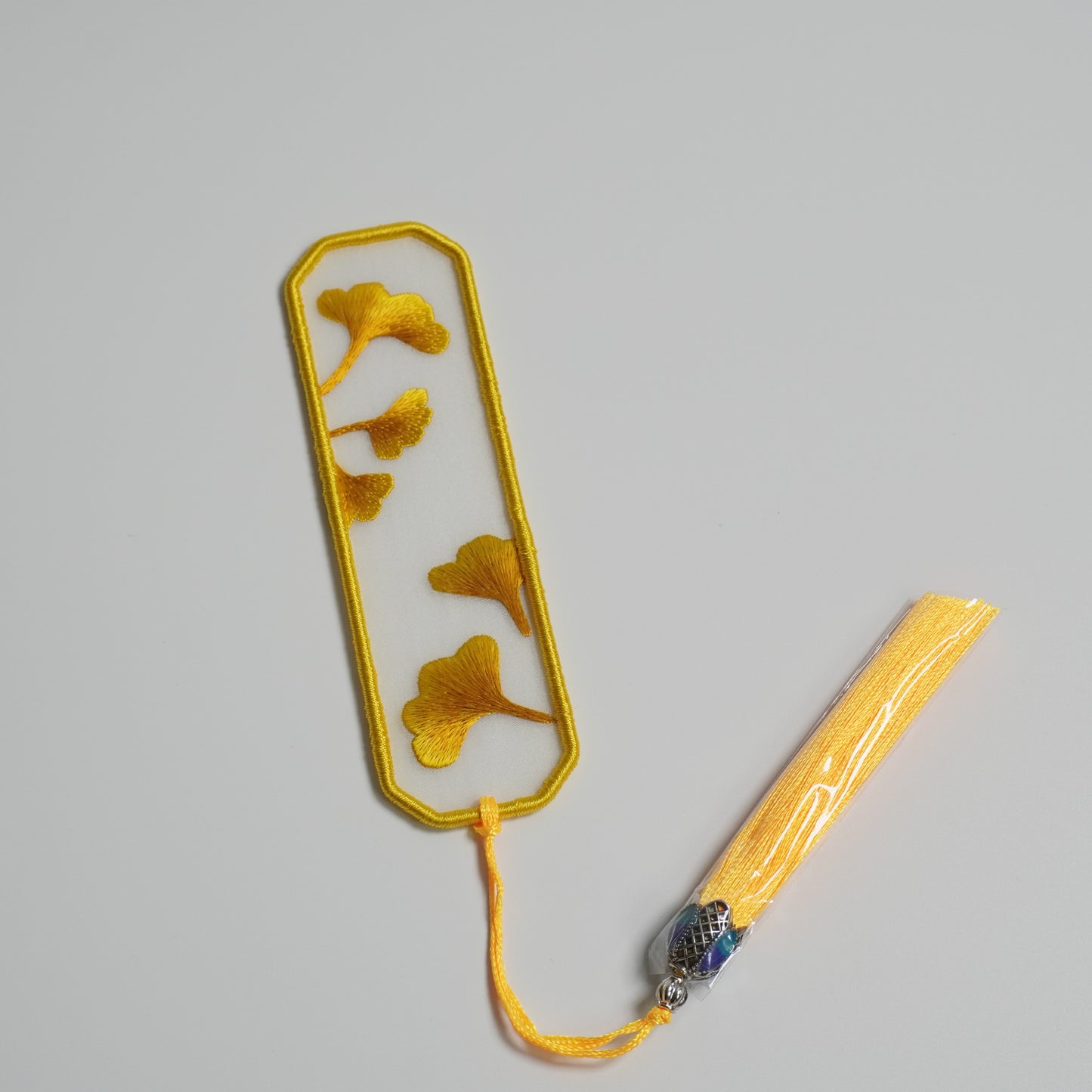 Hand-embroidered ginkgo leaf bookmark on silk with olive yellow tassel. 