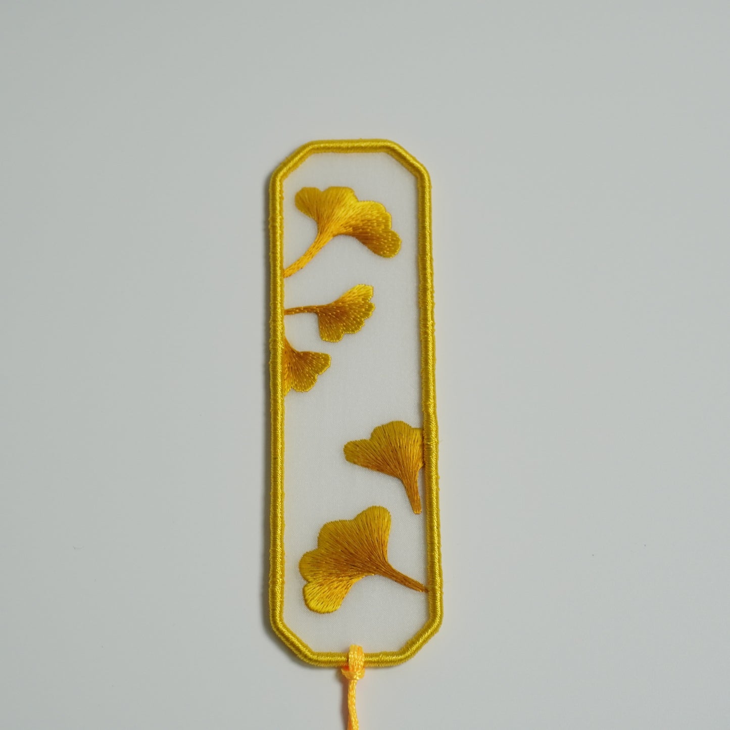 Close-up hand-embroidered ginkgo leaf bookmark on silk with olive yellow tassel. Traditional Chinese embroidery craft.