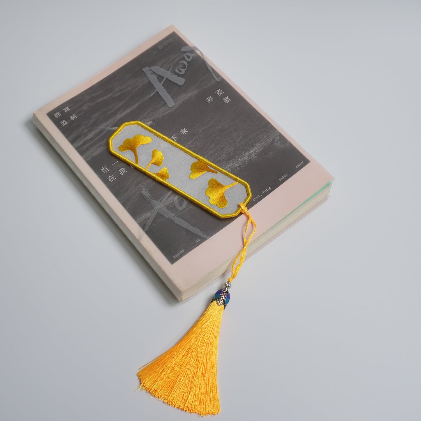 Hand-embroidered ginkgo leaf bookmark on silk with olive yellow tassel. Traditional Chinese embroidery craft.