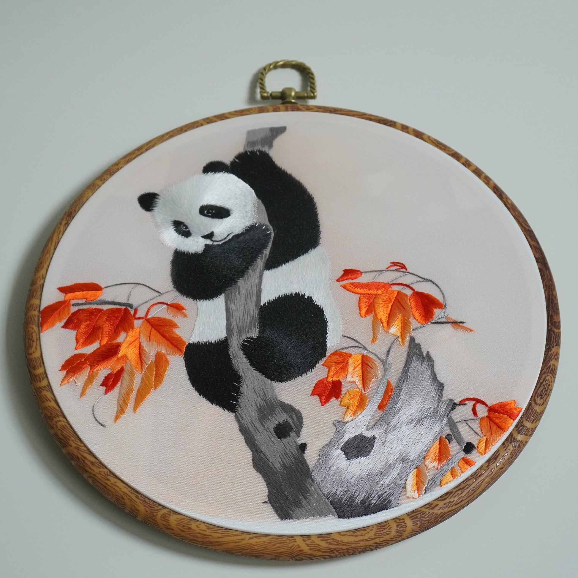 Details of hand-embroidered panda climbing maple tree branch on round faux-wood hoop. 20cm silk embroidery wall art.