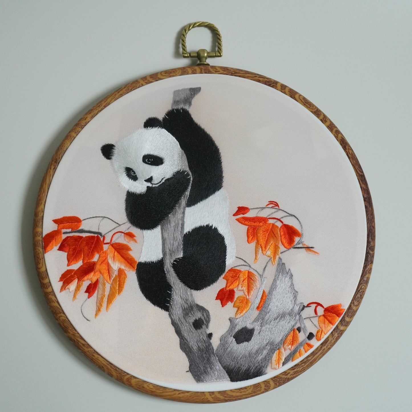 Close-up hand-embroidered panda climbing maple tree branch on round faux-wood hoop. 20cm silk embroidery wall art.